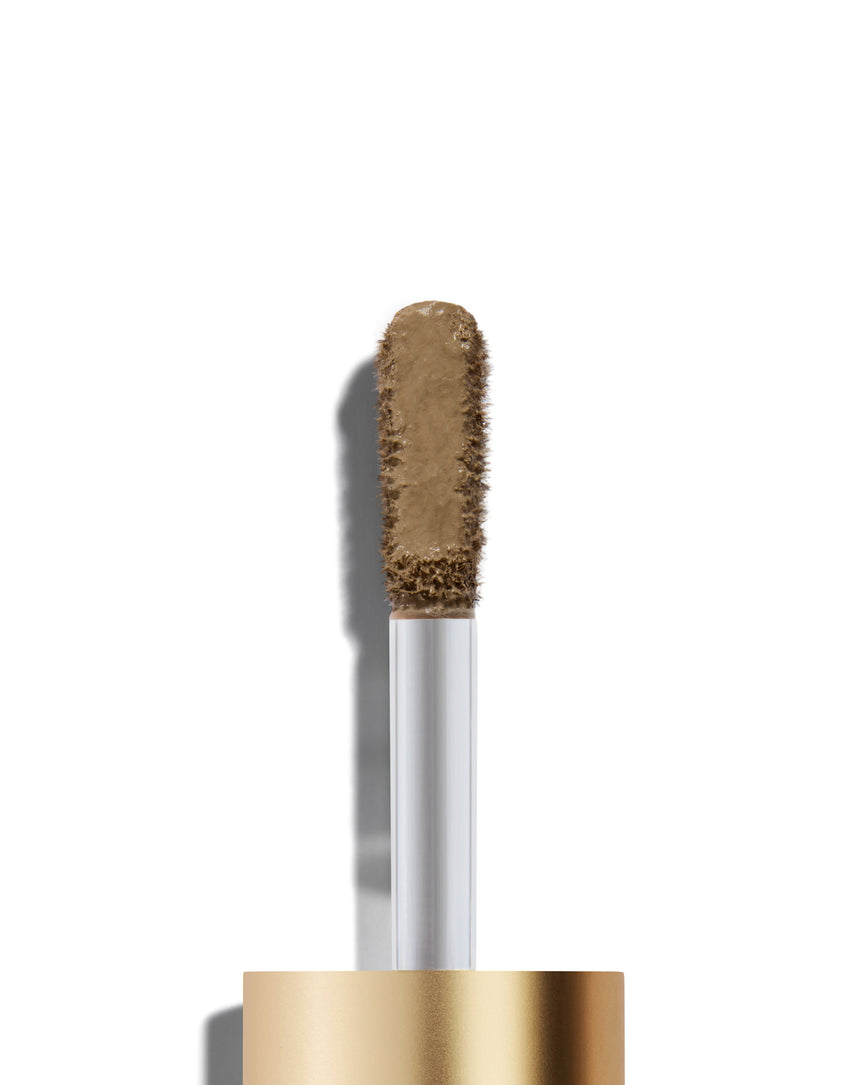 The end of a gold cap containing an applicator wand with a Mimi Liquid Silk eyeshadow on it, against a white background.