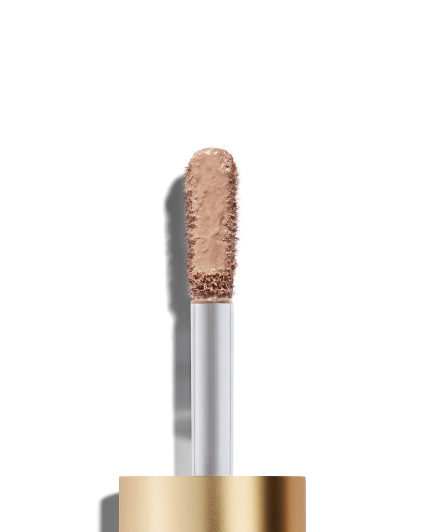 The end of a gold cap containing an applicator wand with a Paige Liquid Silk eyeshadow on it, against a white background.