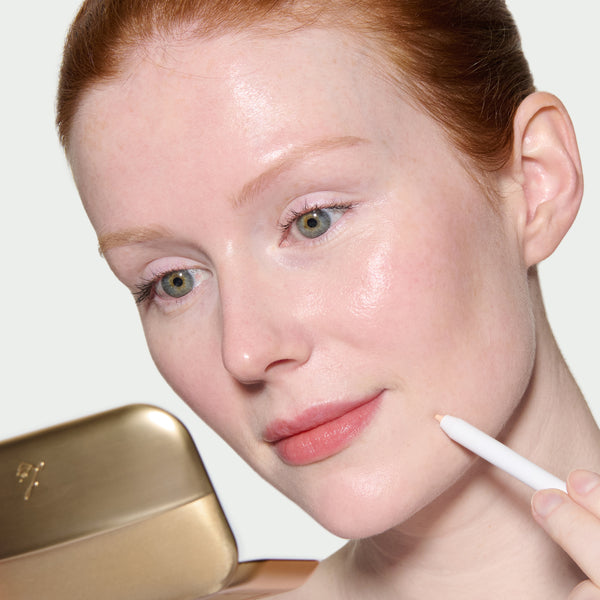 Close-up of a model's face with her applying Pinpoint Concealer using The Eyeshadow Palettes compact mirror