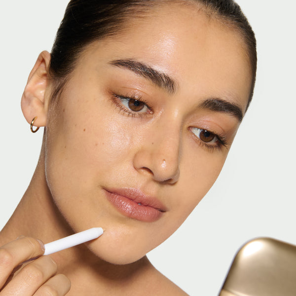 Close-up of a model's face with her applying Pinpoint Concealer using The Eyeshadow Palettes compact mirror