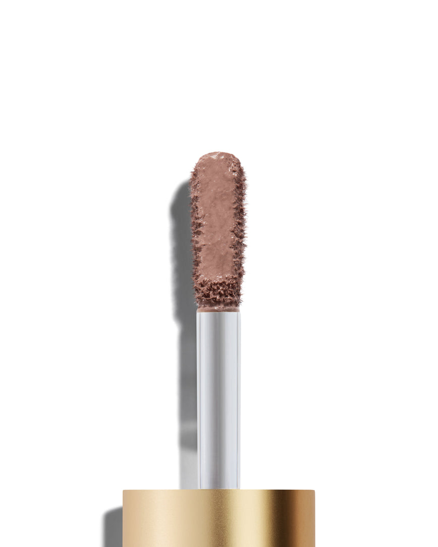 The end of a gold cap containing an applicator wand with a Silvia Liquid Silk eyeshadow on it, against a white background.