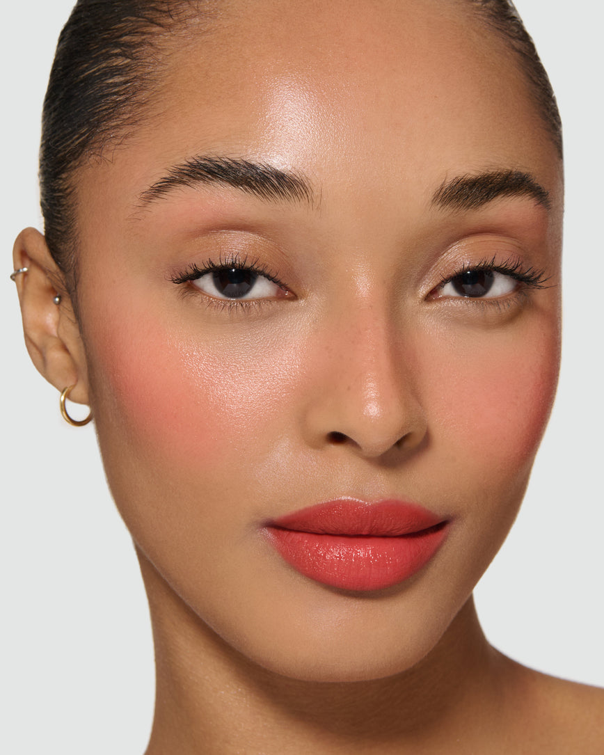 Close-up of a model's face with a neutral background, wearing Velatura Balm in shade Pomegranate Glace