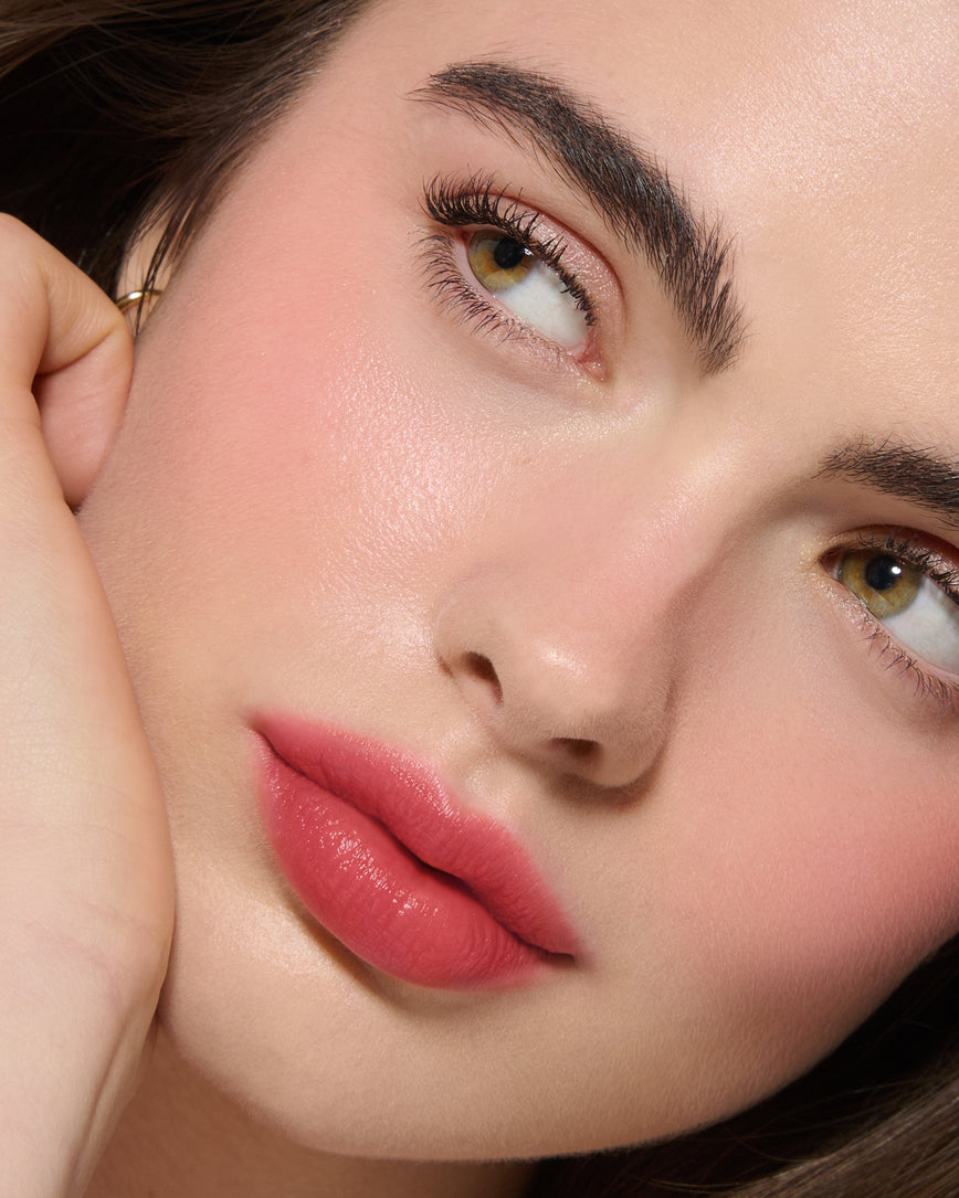 Extreme Close-up of a model's face with a neutral background, wearing Pomegranate Glace Velatura Balm on lip and cheeks