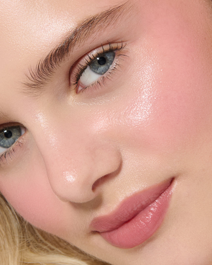 Close-up of a model's face with a neutral background, wearing Rose Madder Velatura Balm on lip and cheeks