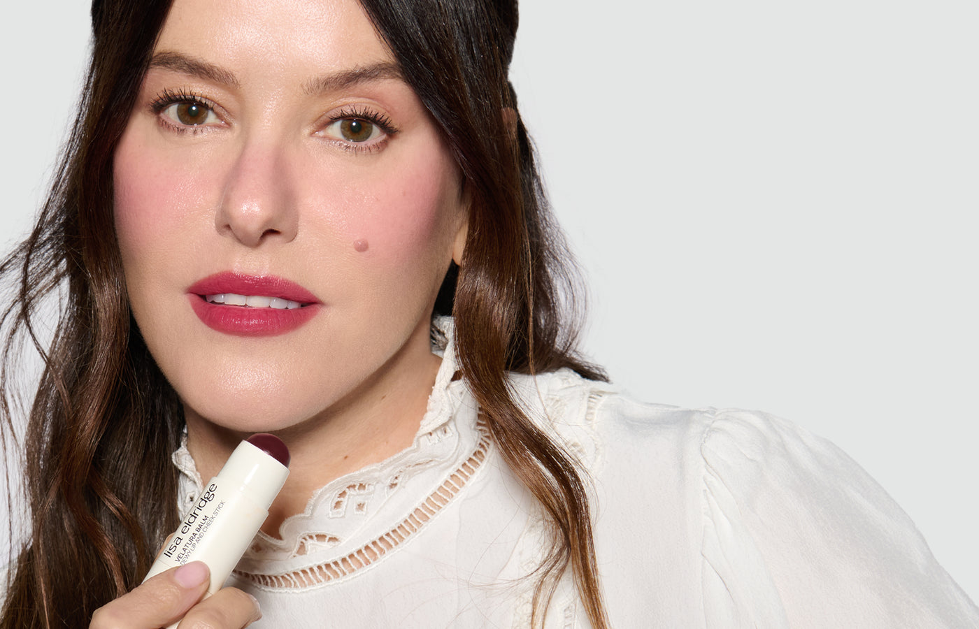 Lisa holding a Veltura Balm Dewy Lip and Cheek Stick in Hellebore Heaven with a neutral background