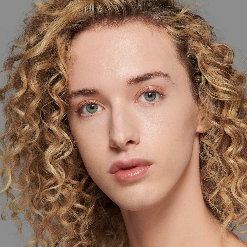 Lisa Eldridge Seamless Skin Foundation Pictured on Model. A young model with light skin and peach undertones, green eyes and curly dark blonde hair. The text says ‘No.4 With Peach Undertones'
